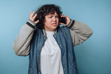 A person with curly hair looks frustrated while talking on a smartphone against a blue background.