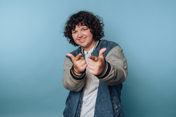  person with curly hair wearing a denim jacket and a white shirt, posing playfully against a light...
