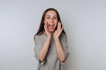 A cheerful woman with long brown hair wearing a gray shirt, expressing excitement with her hands...