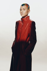 woman with colorful short hair wearing a red leather coat, standing with hands in pockets against...