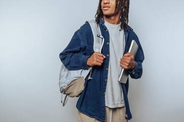 Young person with backpack and laptop, casual attire, neutral background.
