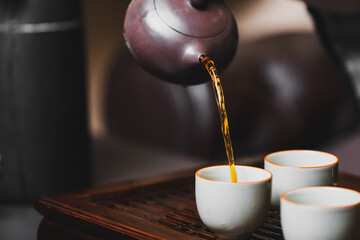Close-up of hot tea being poured from a traditional teapot into a white ceramic cup on a wooden...