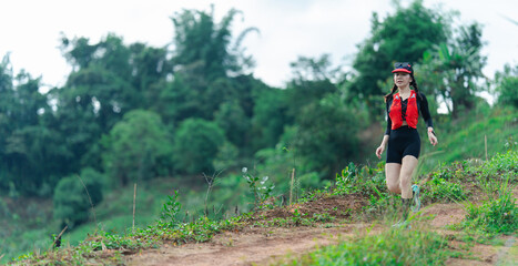 A woman in athletic gear runs along a dirt trail surrounded by greenery and trees under a partly...