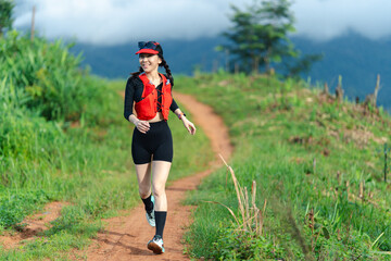A woman runs on a dirt trail surrounded by greenery and hills, wearing athletic gear and sunglasses...
