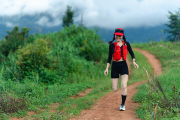 A woman in sporty attire runs joyfully on a dirt trail surrounded by lush greenery and misty...