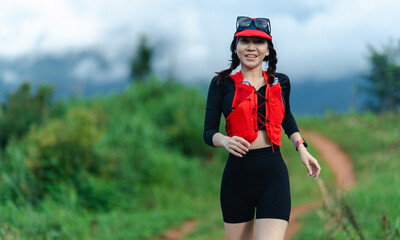 A woman wearing a red vest and black athletic outfit is jogging outdoors on a trail surrounded by...