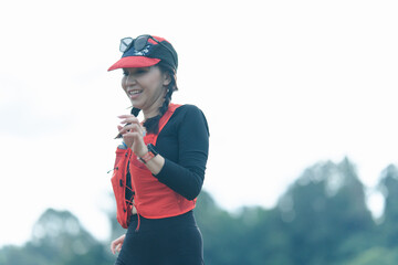 A woman in athletic gear jogs outdoors, smiling, wearing a red visor and sunglasses on her head with a natural blurred background.