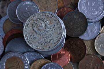 Close up of Soviet Union commemorative coin with coat of arms on obverse, uncirculated coin with dents and corrosion against other coins blurred in background