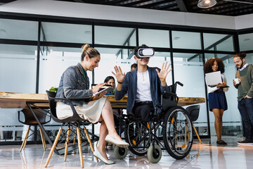 latin young man in wheelchair using virtual reality glasses at office in Mexico Latin America, hispanic coworkers or teamwork in concept of disability and social inclusion using vr technology