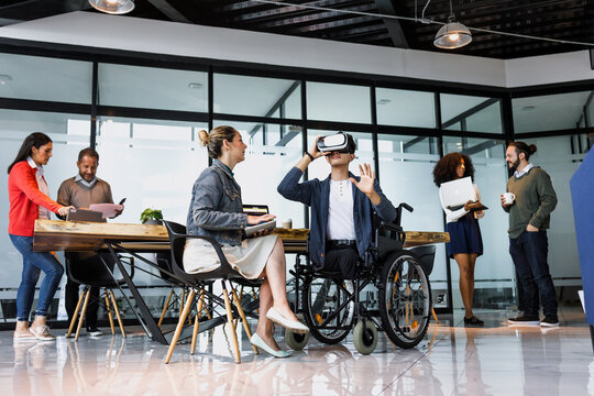 latin young man in wheelchair using virtual reality glasses at office in Mexico Latin America, hispanic coworkers or teamwork in concept of disability and social inclusion using vr technology - Powered by Adobe