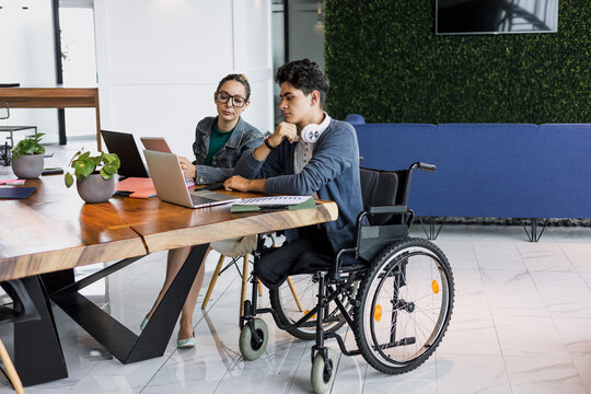 Latin young man in wheelchair working at office in Mexico Latin America, hispanic coworkers and business teamwork in concept of disability and disabled person - Powered by Adobe
