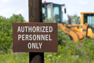 authorized personnel only sign next to construction site with bulldozer vehicle in the background (do not enter work zone forbidden prohibited entry hard hat danger dangerous area) industrial zone
