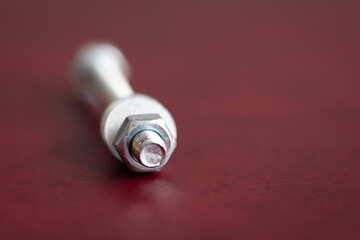 Bolt isolated on dark red background, laying down with nut and washer in front and head is out of focus