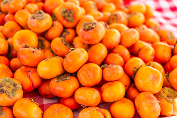 A vibrant display of fresh persimmon fruit arranged neatly for sale at a farmers market, highlighting seasonal produce and tactile interaction with food.