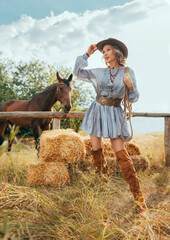 photo real person cowgirl with horse holds lasso rope. bale of hay dry grass straw field nature summer. Happy face Woman ranch owner in leather hat boots. sexy Girl blue short dress cowboy style belt