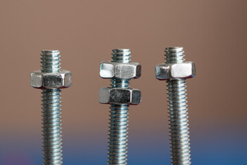 Three bolts with nuts isolated on background, middle one has two nuts and others one