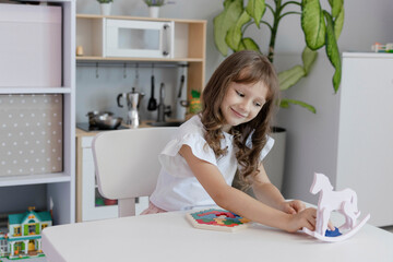 The kid girl is playing board educational game at the table in the children's room. The concept of child development. The concept of leisure for children