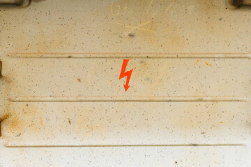 Red high voltage lightning warning sign painted on a dusty industrial metal surface. Electrical hazard safety symbol
