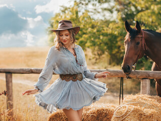 fashion model posing with horse pet dancing. field nature summer sky bale of hay dry grass straw. Happy face lady. Woman ranch owner in leather brown hat boots. cowgirl sexy Girl blue short dress fly