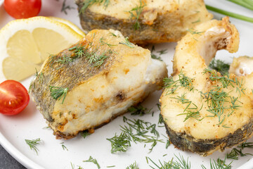Baked zander fish with lemon, dill and cherry tomato on white ceramic plate closeup. Fried...