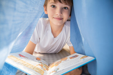 Smiling boy reading a book under a fabric tent