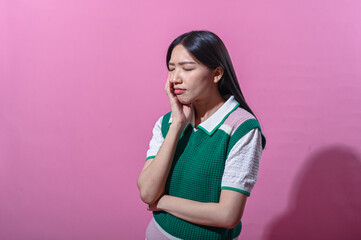 Asian woman in a green and pink sweater vest with a thoughtful expression, eyes closed and hand on...