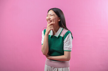 Asian woman in a green and pink sweater vest with a thoughtful expression, eyes closed and hand on...