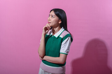 Asian woman in a green and pink sweater vest with a thoughtful expression, eyes closed and hand on...