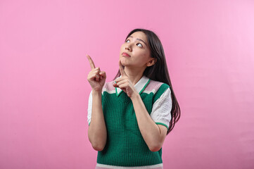 Asian woman smiling while pointing to the right with both hands, wearing a green and pink knit top,...
