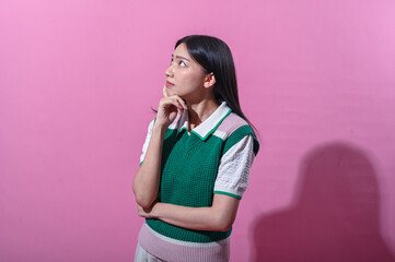 Asian woman in a green and pink sweater vest with a thoughtful expression, eyes closed and hand on...