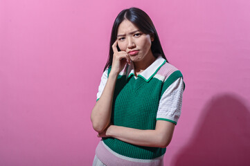 Asian woman in a green and pink sweater vest with a thoughtful expression, eyes closed and hand on...