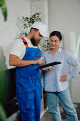 Technician smiling while demonstrating repair details to homeowner on tablet inside. Concept of technician explaining AC functions, HVAC service feedback, residential client satisfaction