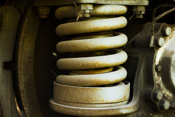 Macro shot of a rusty metal coil spring from an industrial or railway suspension system. The aged surface, dirt, and cobwebs emphasize wear, time, and mechanical reliability