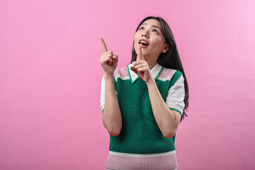 Asian woman smiling while pointing to the right with both hands, wearing a green and pink knit top,...