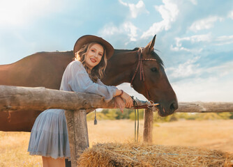 photo real person cowgirl with horse, field nature summer sky sun light day. Woman rider in leather hat. Smiling face blonde sexy Girl in blue short dress wild west country style. pen, wooden fence