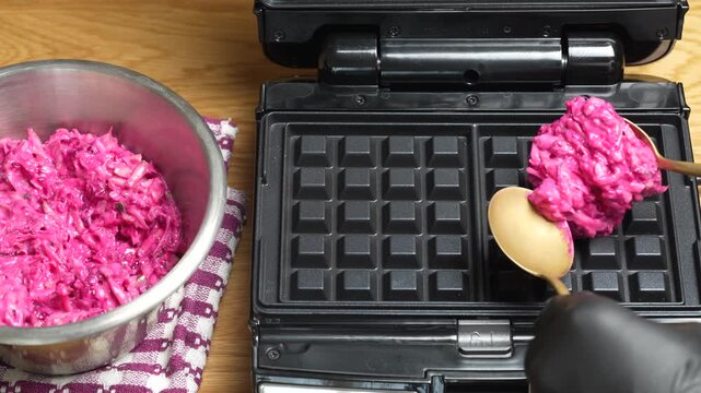 Making vegetarian beetroot and zucchini waffles with herbs in waffle maker, close up. Vegetable waffles for eat made with waffle iron with teflon coating