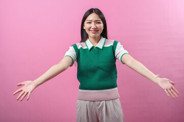 Asian woman smiling warmly with arms wide open as if offering a hug, wearing a green knit vest,...