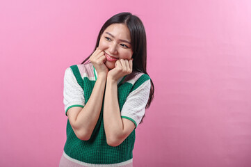 Asian woman with a playful expression poses with clenched fists under her chin, wearing a green...