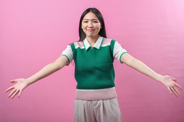 Asian woman smiling warmly with arms wide open as if offering a hug, wearing a green knit vest,...
