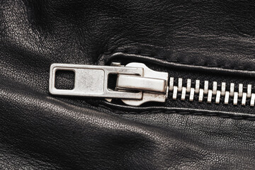 Metal zipper on black leather. Closeup view of clothing detail. Shiny silver fastener on textured...