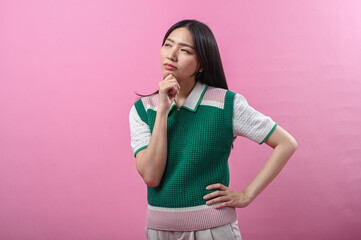 Asian woman in a green sweater posing with a thinking gesture, resting her chin on her hand while...