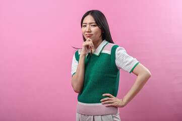 Asian woman in a green sweater posing with a thinking gesture, resting her chin on her hand while...