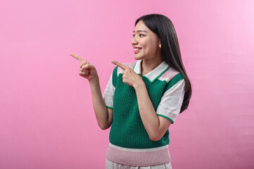 Asian woman smiling while pointing to the right with both hands, wearing a green and pink knit top,...