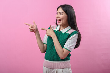 Asian woman smiling while pointing to the right with both hands, wearing a green and pink knit top,...