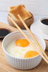 Half-boiled eggs in bowl, soy sauce, chopsticks, coffee and toasted bread on light grey table, closeup. Traditional asian breakfast