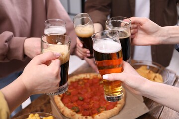 Friends clinking glasses of beer at wooden table, closeup