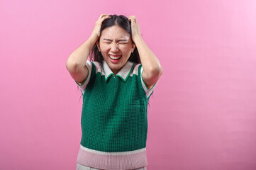 Asian woman pulling her hair in frustration and closing her eyes tightly, expressing extreme stress...