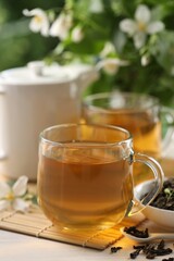 Tasty jasmine tea in cups, teapot, dry leaves and flowers at white wooden table, closeup