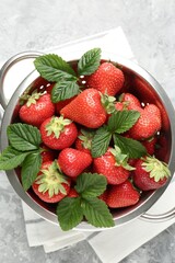 Delicious ripe strawberries and green leaves in colander on grey table, top view