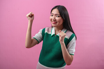 Asian woman celebrating with joyful expression, both fists clenched in excitement, smiling...